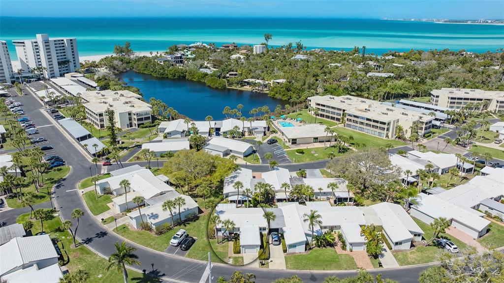An aerial view of a coastal residential complex featuring white buildings, a lake, and beach — 119 WHISPERING SANDS CIRCLE UNIT V36, SARASOTA, FL