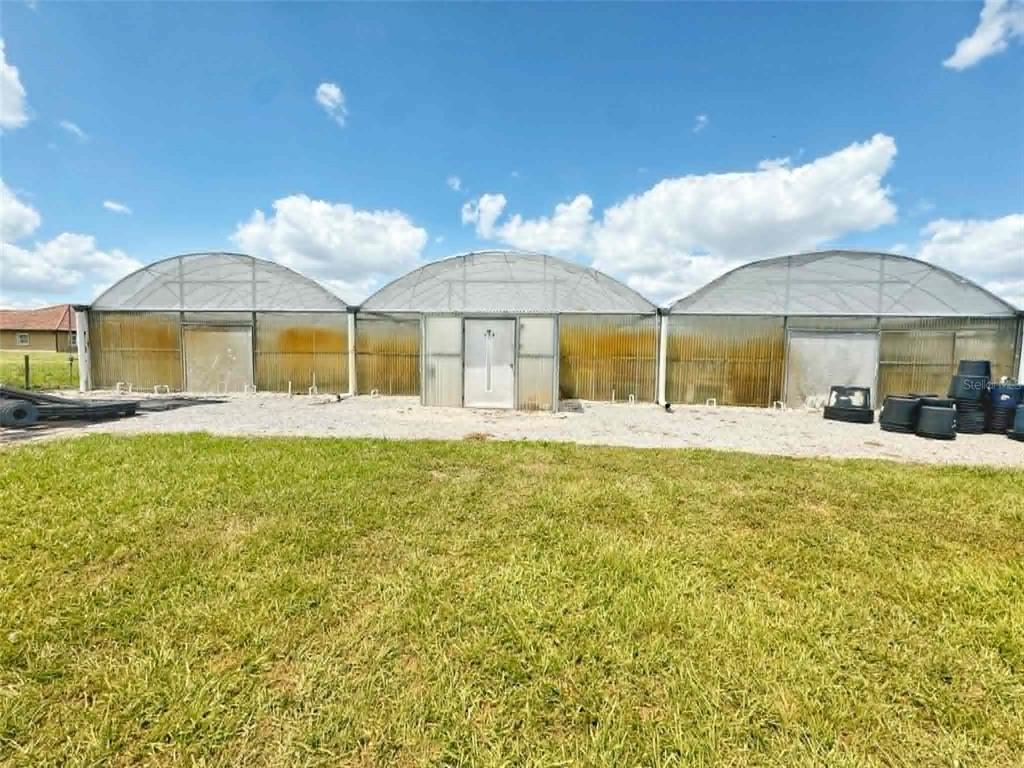 A exterior view of a three-bay greenhouse structure with arched roofs and a central door — 612 MORGAN ROAD, WINTER HAVEN, FL
