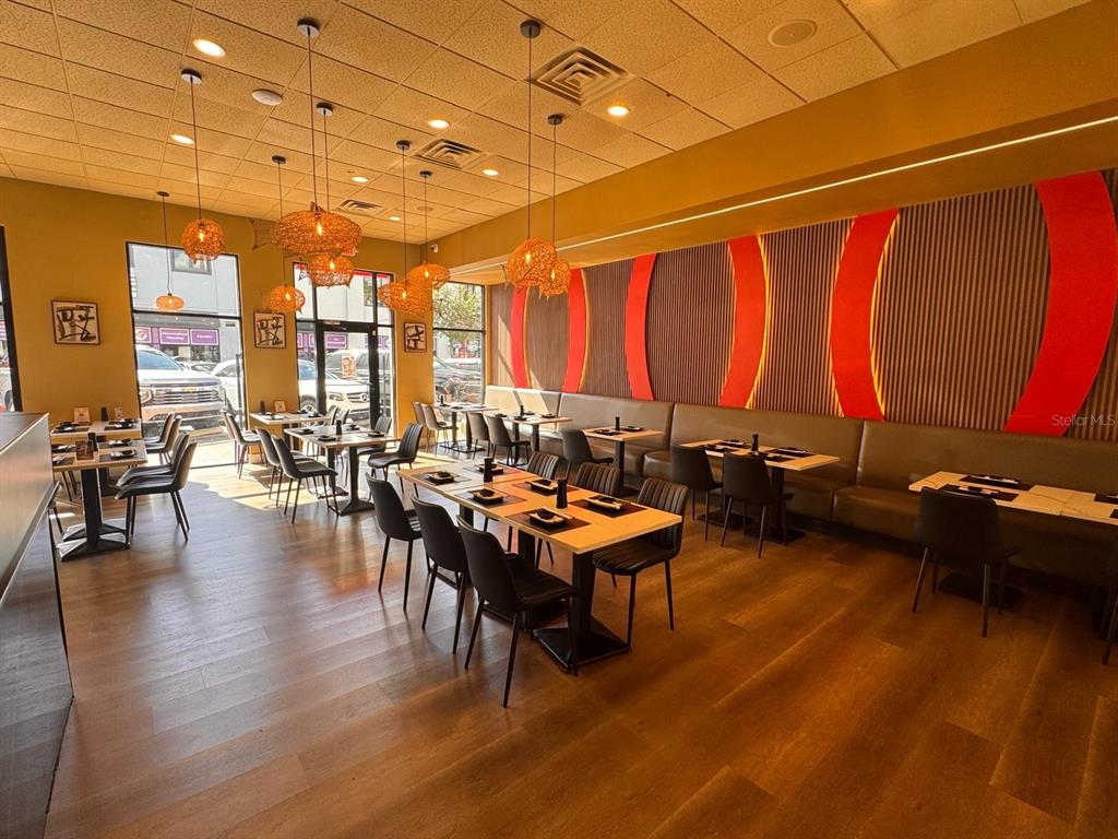 A restaurant dining room features wooden floors, pendant lights, and a long banquette seating area — 9664 W LINEBAUGH AVE, TAMPA, FL
