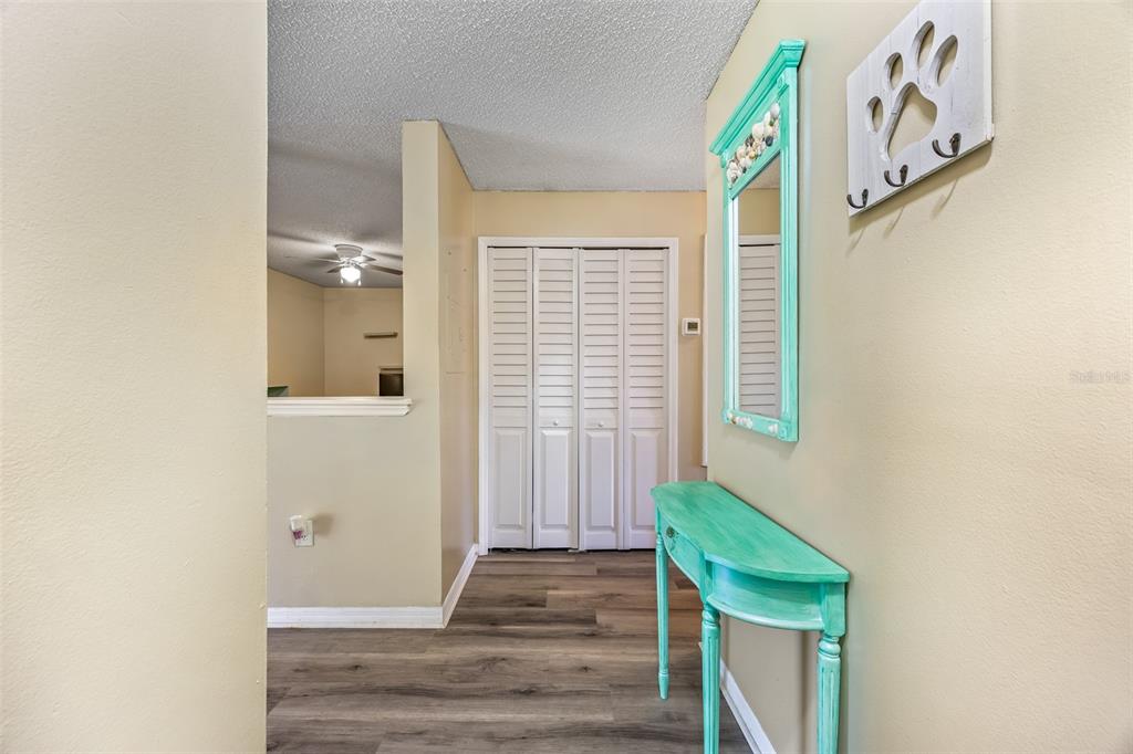 An entryway features wood-look flooring, a turquoise console table, a matching mirror, and bi-fold closet doors — 275 SPRING DRIVE UNIT 4, MERRITT ISLAND, FL