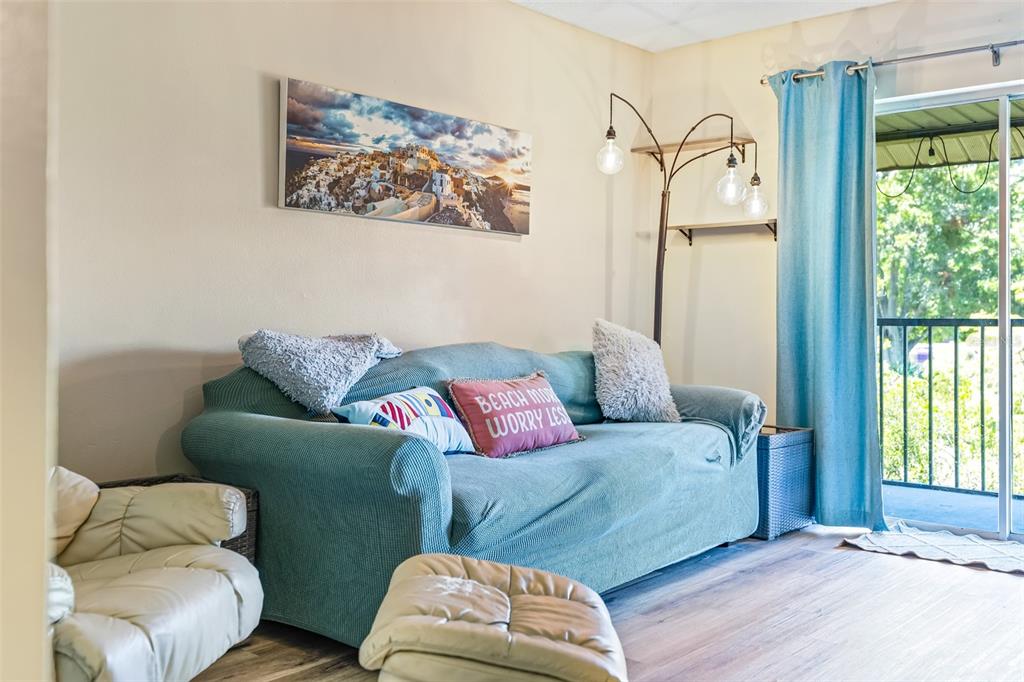 A living room features a teal sofa, a white armchair, and a sliding glass door — 275 SPRING DRIVE UNIT 4, MERRITT ISLAND, FL