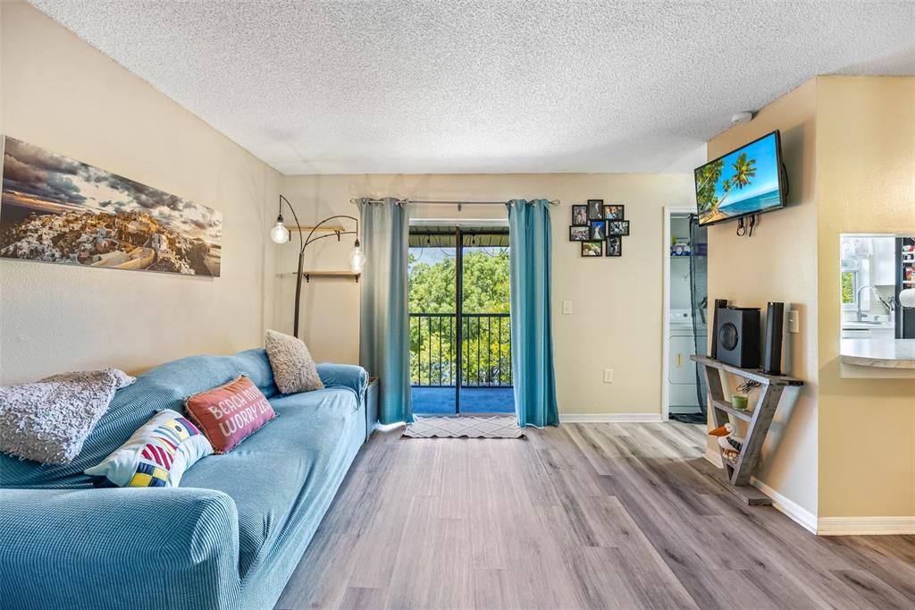 A living room features a blue sofa, wood-look flooring, and a sliding glass door balcony — 275 SPRING DRIVE UNIT 4, MERRITT ISLAND, FL