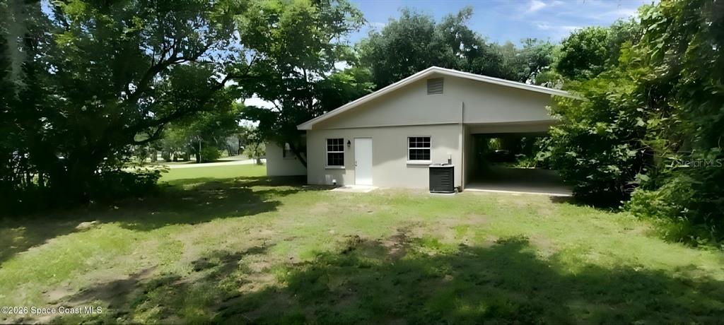 The exterior of a light-colored house features a side carport and a grassy yard — 3509 BREVARD ROAD, MIMS, FL