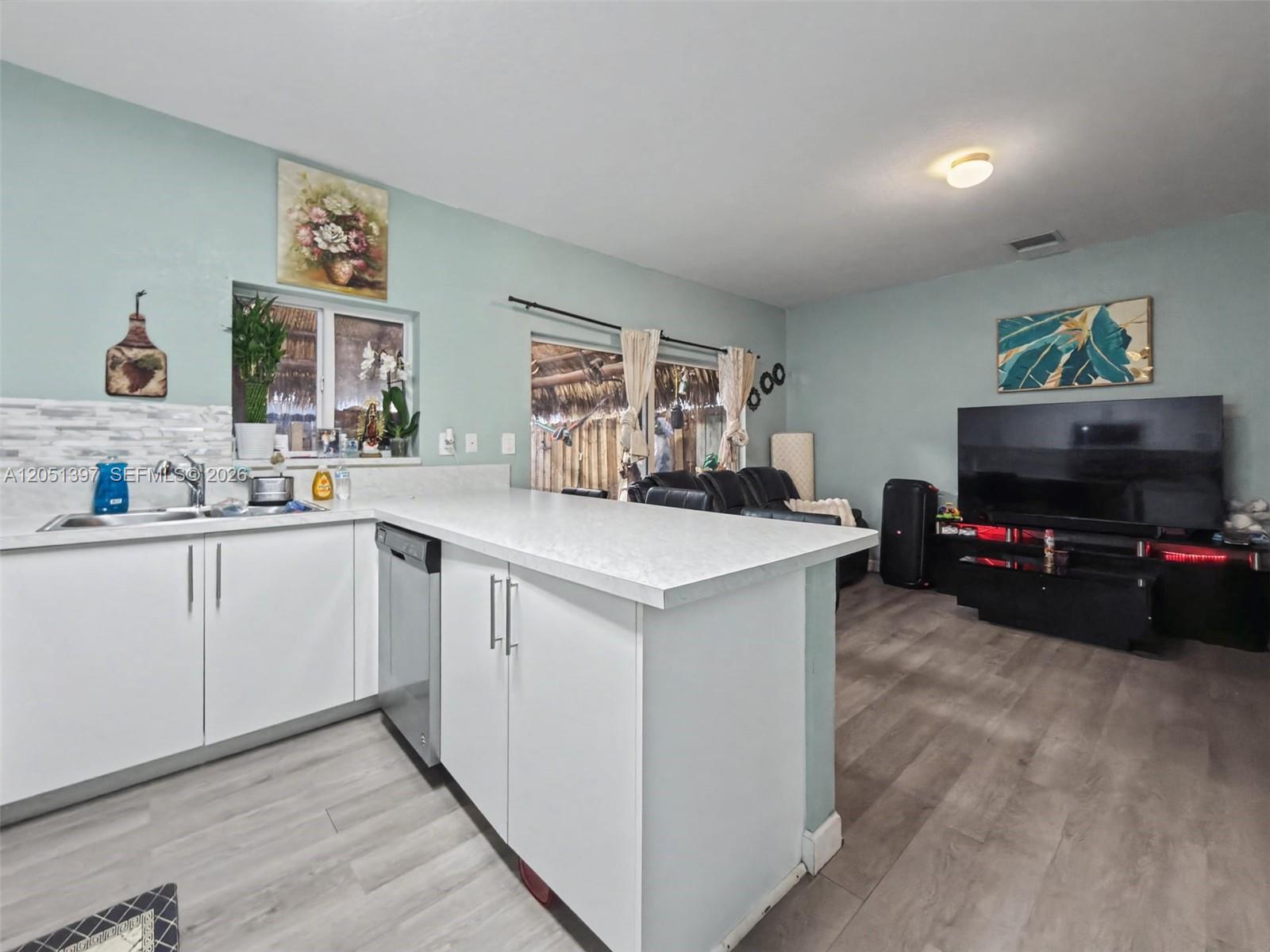 A kitchen with white cabinets and a peninsula opens into a living area with flooring — 396 NW 12th Pl, Florida City FL 33034, FLORIDA CITY, FL