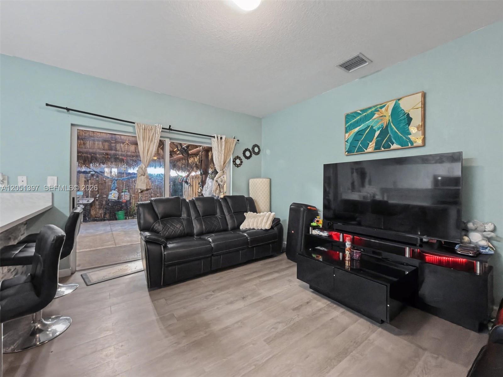 A living room features light blue walls, wood-look flooring, a black sofa, and a sliding door — 396 NW 12th Pl, Florida City FL 33034, FLORIDA CITY, FL