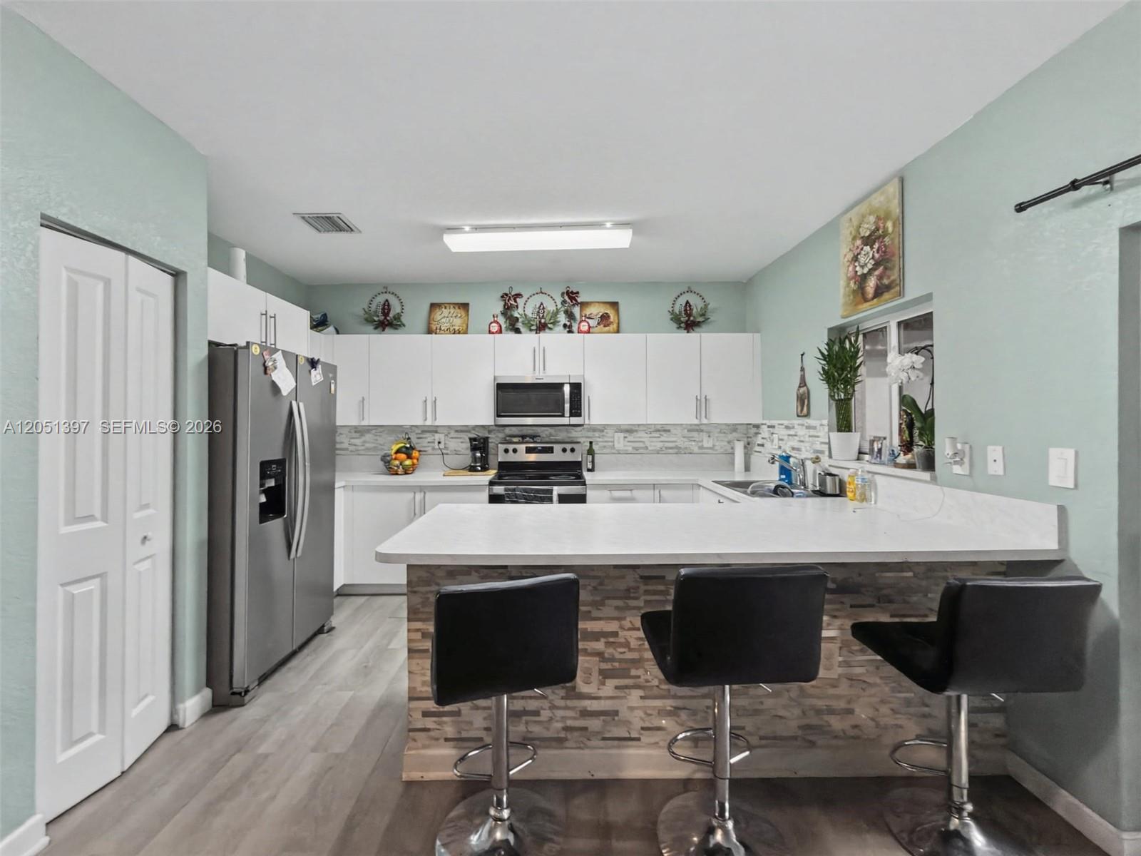 A kitchen features white cabinets, stainless steel appliances, a stone-accented breakfast bar, and stools — 396 NW 12th Pl, Florida City FL 33034, FLORIDA CITY, FL