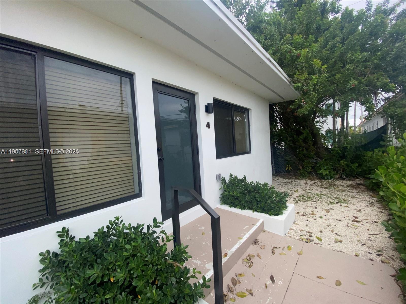 The exterior of a white building features a black-framed door, windows, and a small porch — 1765 Normandy Dr, Miami Beach FL 33141, MIAMI BEACH, FL