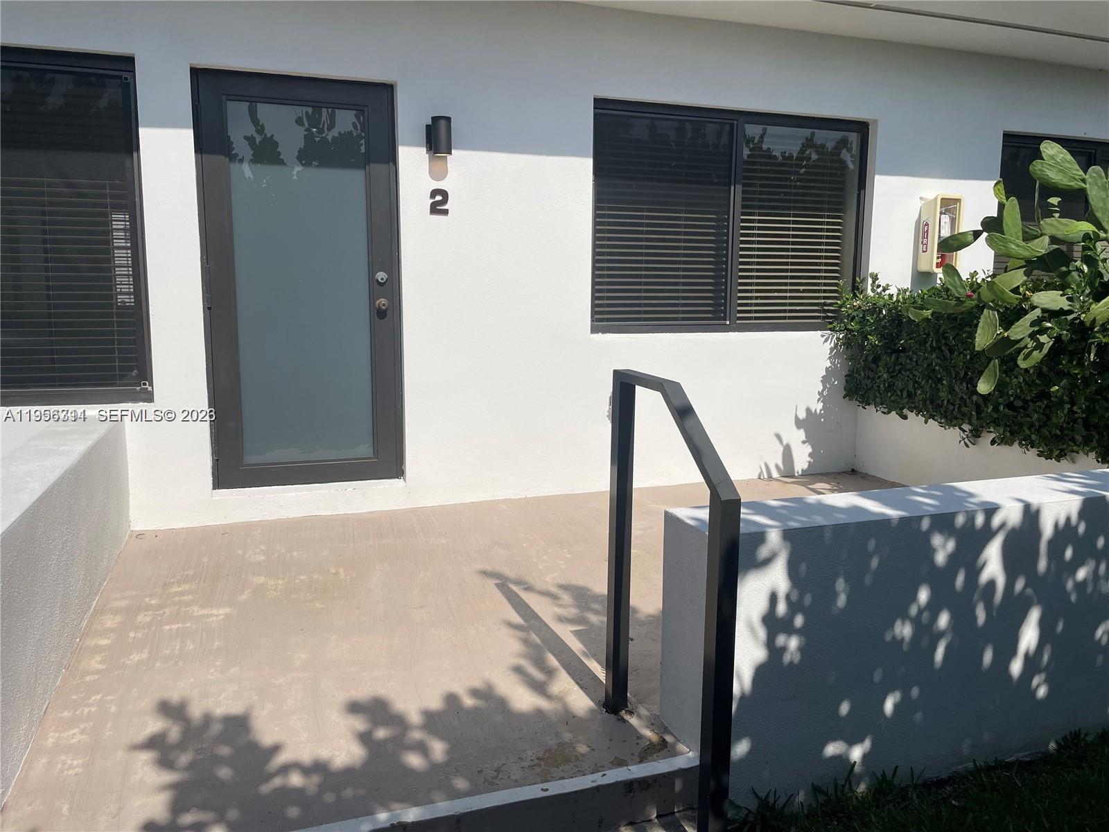 A white exterior wall features a dark-framed glass door labeled number two and windows — 1765 Normandy Dr, Miami Beach FL 33141, MIAMI BEACH, FL