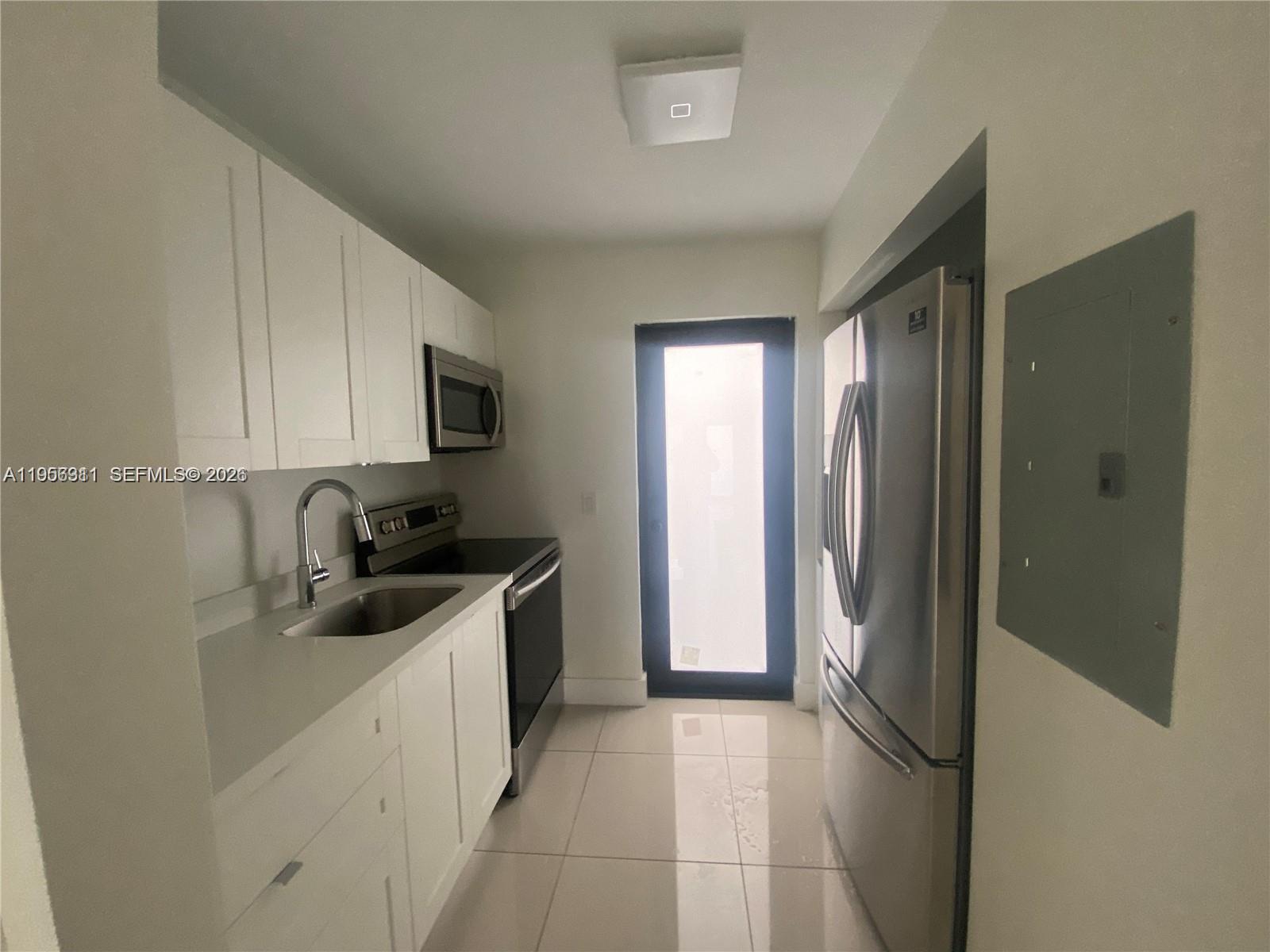 A galley kitchen features white cabinets, stainless steel appliances, a sink, and light tile flooring — 1765 Normandy Dr, Miami Beach FL 33141, MIAMI BEACH, FL