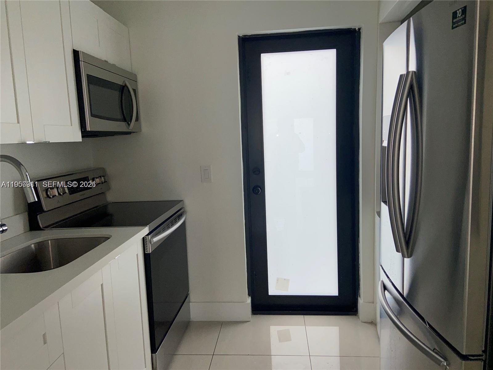A compact kitchen features white cabinets, stainless steel appliances, and a black-framed glass door — 1765 Normandy Dr, Miami Beach FL 33141, MIAMI BEACH, FL