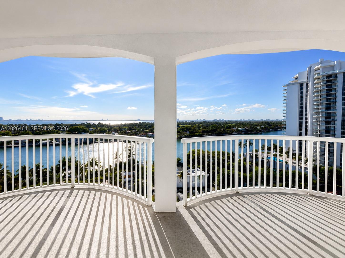 A balcony with white railings overlooks a waterfront view and a neighboring high-rise building — 5401 Collins Ave # 1022, Miami Beach FL 33140, MIAMI BEACH, FL