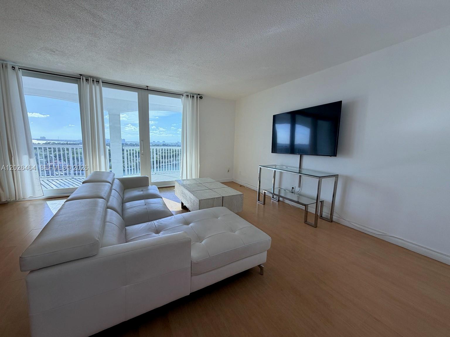 A living room features a white sectional sofa, a glass console table, and a balcony — 5401 Collins Ave # 1022, Miami Beach FL 33140, MIAMI BEACH, FL