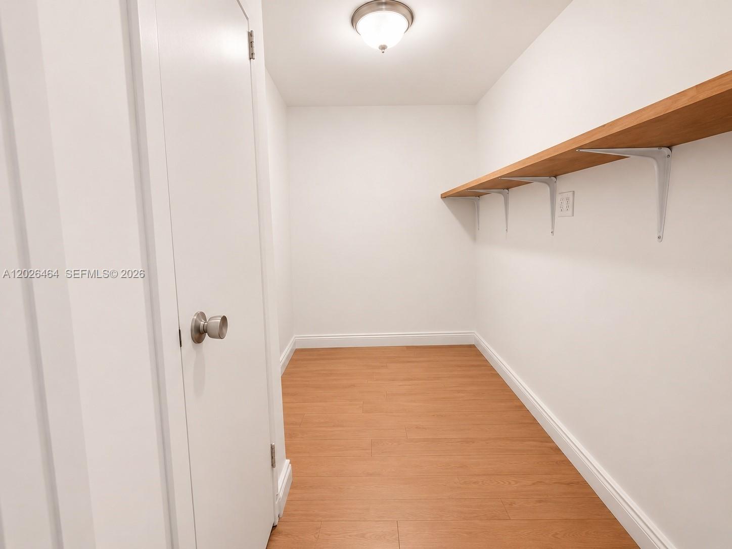 A small, empty closet features wood-look flooring, white walls, and a single wooden shelf — 5401 Collins Ave # 1022, Miami Beach FL 33140, MIAMI BEACH, FL
