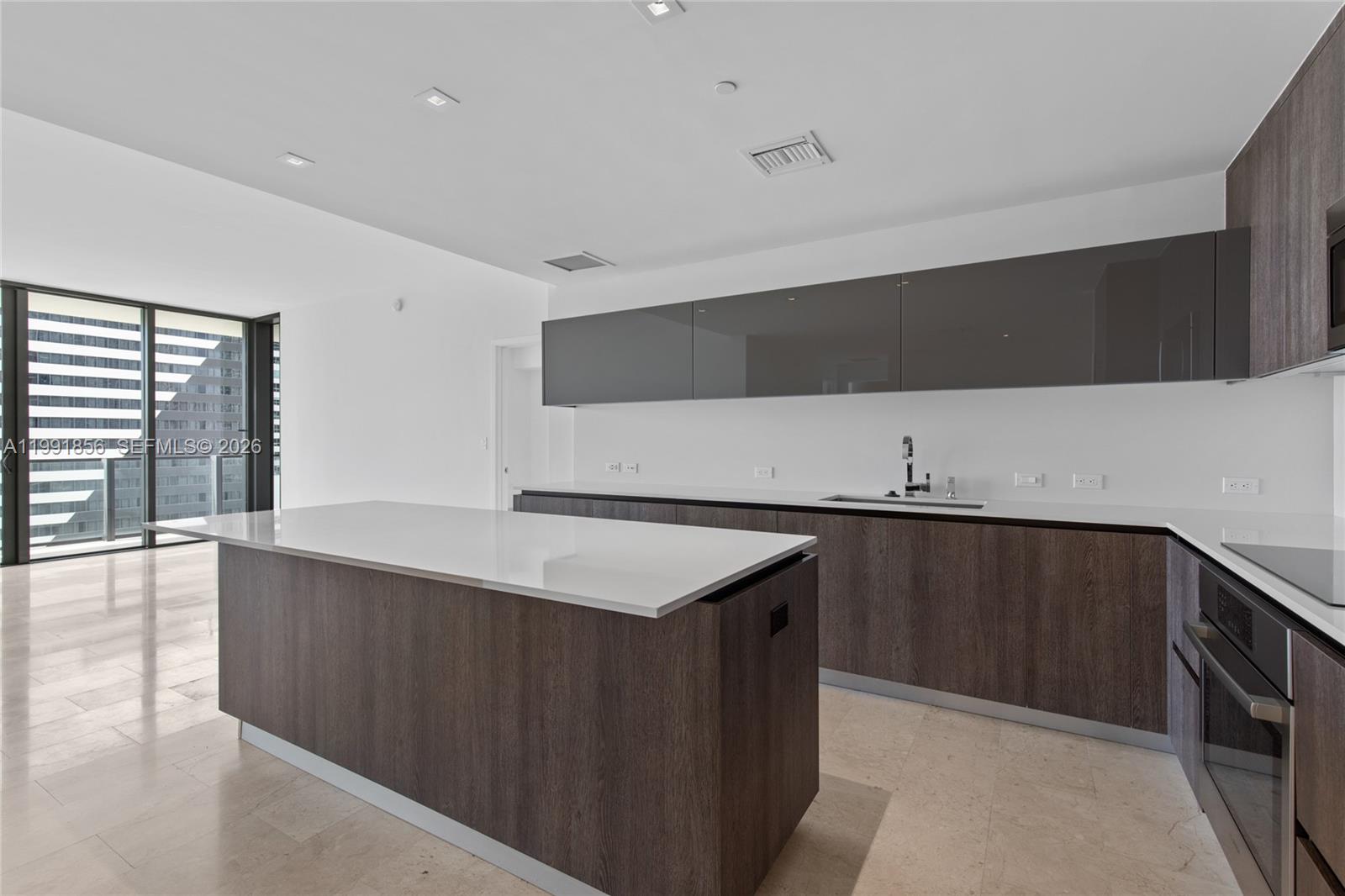 A modern kitchen features dark wood cabinetry, glossy grey upper cabinets, and a white island — 88 SW 7th St # 904, Miami FL 33130, MIAMI, FL