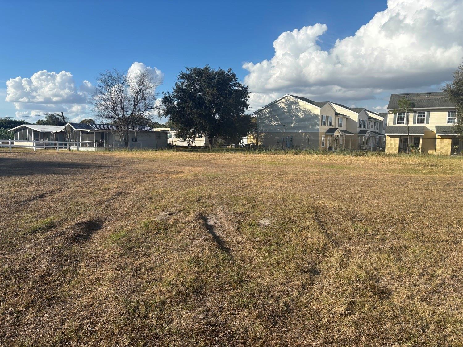 A grassy lot features a white fence and a large tree under a blue sky — 631 SE Us Highway 441, Okeechobee FL 34974, OKEECHOBEE, FL