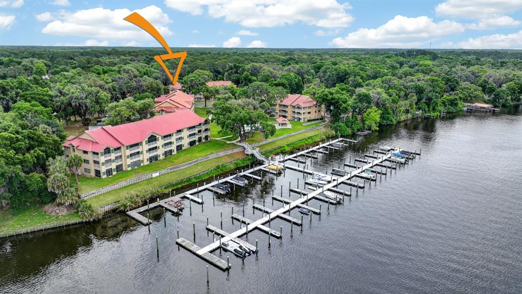 An aerial view shows a multi-story apartment complex with red roofs beside a boat dock — 99 BROAD RIVER PLACE UNIT 2105, WELAKA, FL