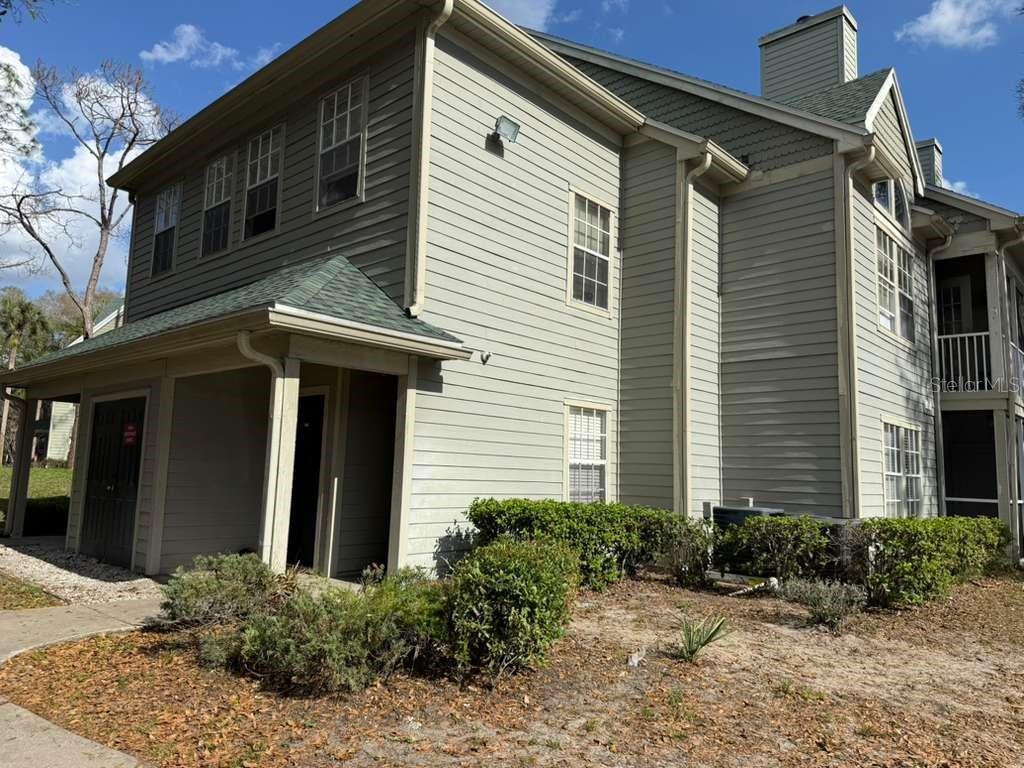 A two-story building with light-colored horizontal siding, a green shingled roof, and a covered entryway — 6094 WESTGATE DRIVE UNIT 101, ORLANDO, FL