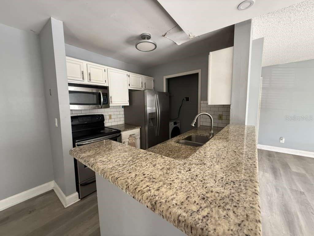 A kitchen features granite countertops, white cabinets, stainless steel appliances, and a breakfast bar — 6094 WESTGATE DRIVE UNIT 101, ORLANDO, FL
