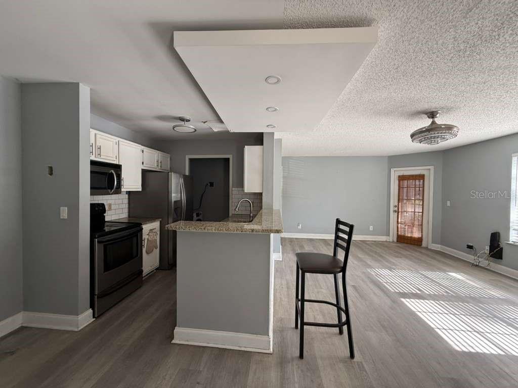A kitchen with a breakfast bar and a large light fixture opens into a living area — 6094 WESTGATE DRIVE UNIT 101, ORLANDO, FL