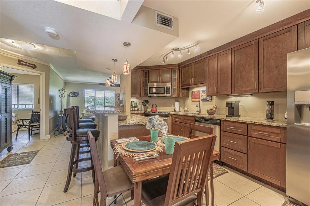 A kitchen with dark wood cabinets, granite countertops, and a dining table in the foreground — 1515 S PINELLAS BAYWAY S S UNIT 29, TIERRA VERDE, FL