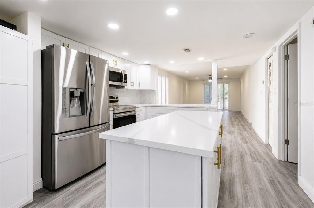 A modern kitchen features white cabinetry, quartz countertops, stainless steel appliances, and a central island — 4965 PURITAN CIRCLE UNIT 401, TAMPA, FL