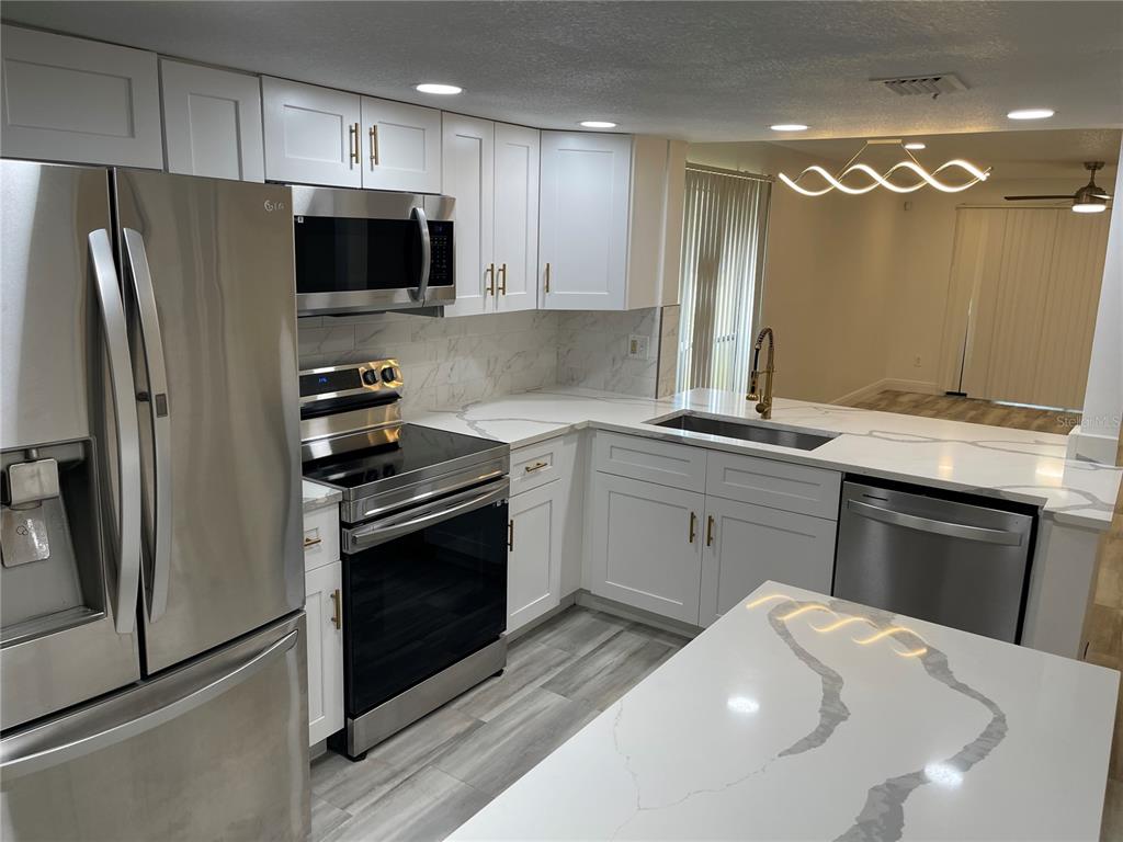 A modern kitchen features white cabinetry, a marble-topped island, stainless steel appliances, and wood-look flooring — 4965 PURITAN CIRCLE UNIT 401, TAMPA, FL