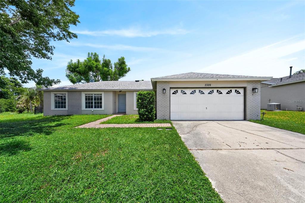 A single-story house with a white garage door, brick facade, and a paved walkway — 2328 CLEMENTINE TRAIL, CLERMONT, FL