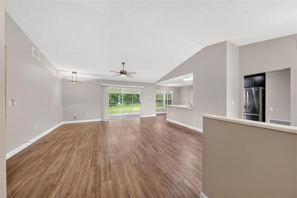 An open-concept living area features wood-look flooring, a ceiling fan, and a sliding glass door — 2328 CLEMENTINE TRAIL, CLERMONT, FL