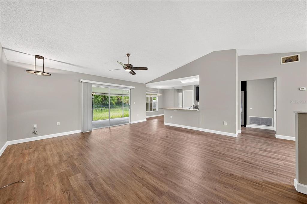 An open-concept living area features wood-look flooring, a vaulted ceiling, and a sliding glass door — 2328 CLEMENTINE TRAIL, CLERMONT, FL