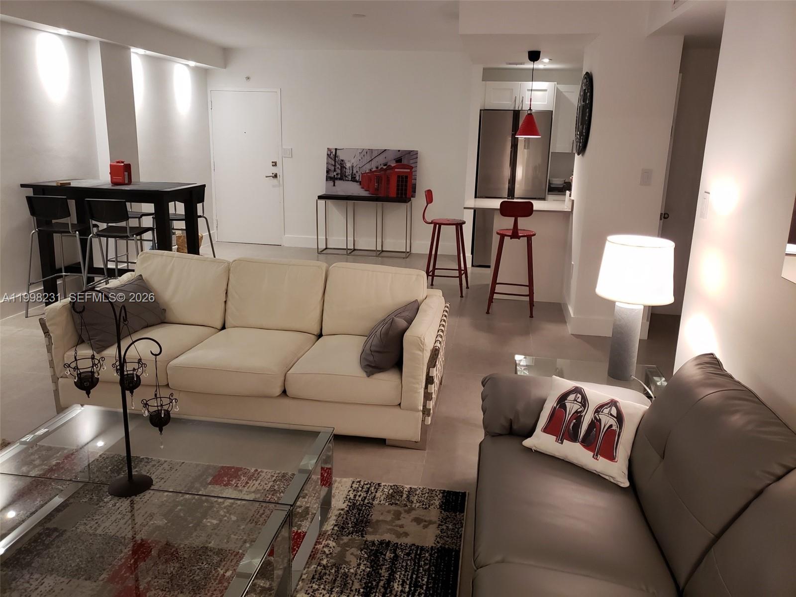 A living room with a white sofa, gray loveseat, glass coffee table, and an open kitchen — 3301 NE 5th Ave # 507, Miami FL 33137, MIAMI, FL