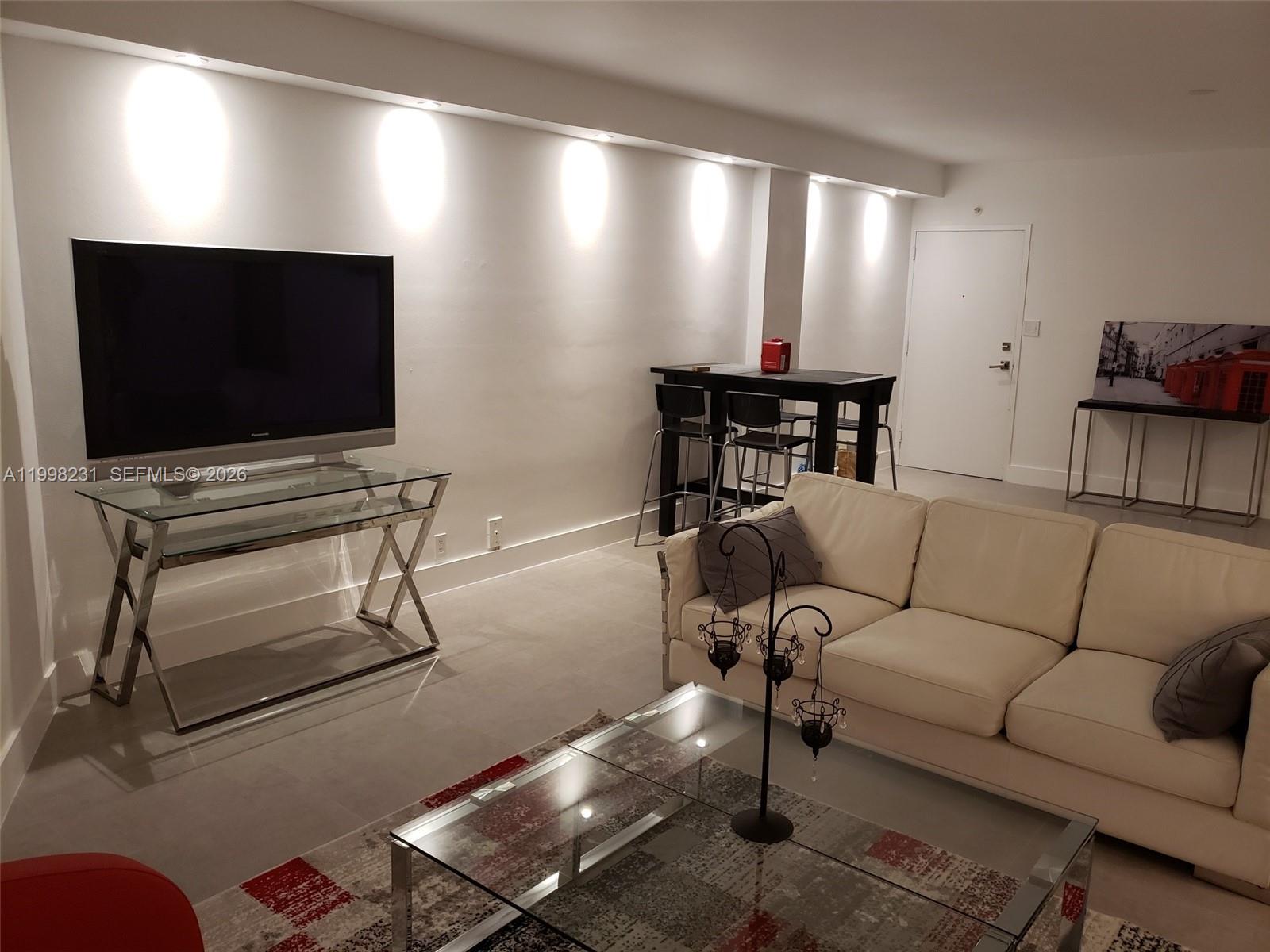 A living room features a white sofa, glass coffee table, and a television on a stand — 3301 NE 5th Ave # 507, Miami FL 33137, MIAMI, FL