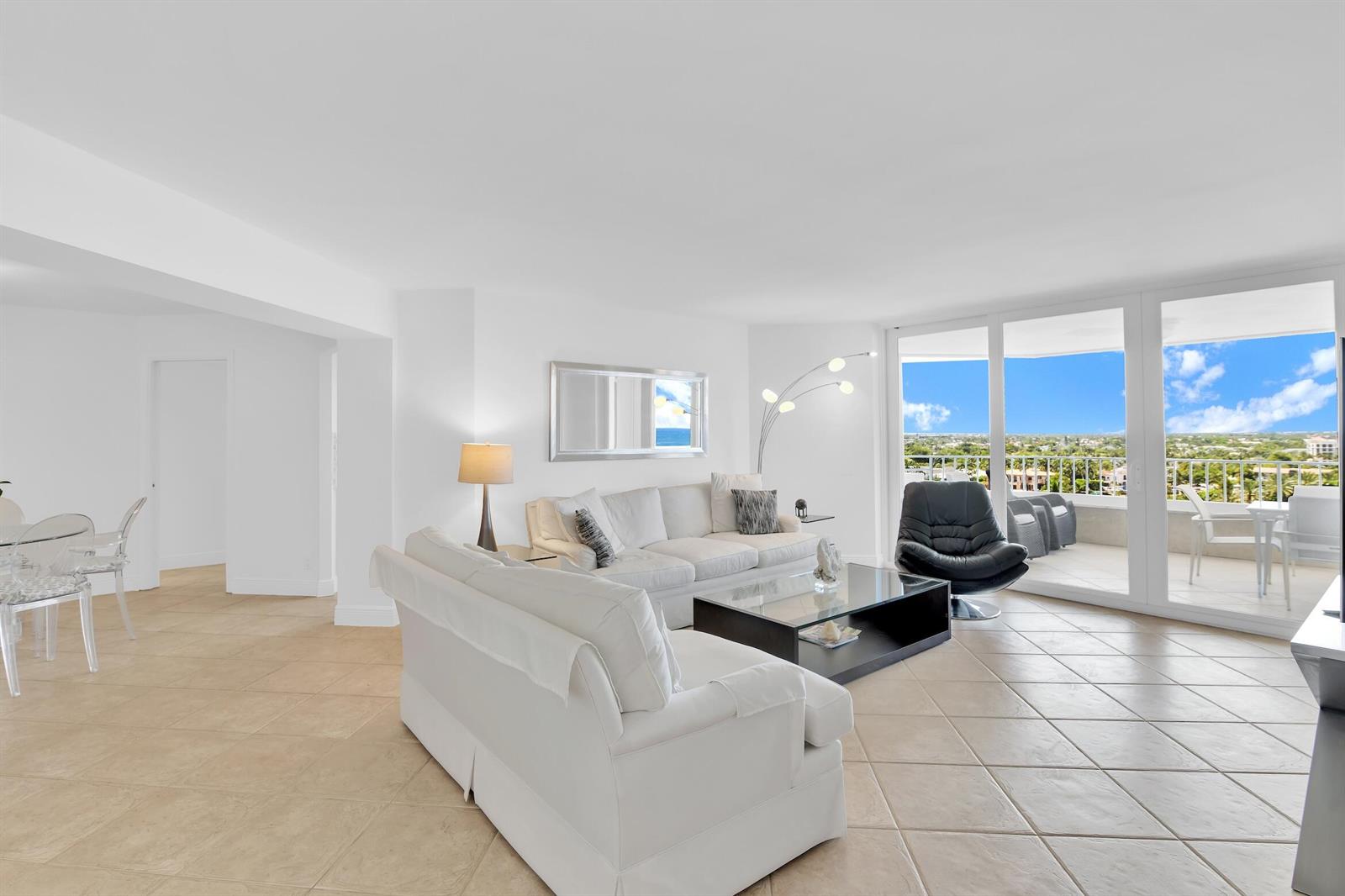 A bright living room features white furniture, tile flooring, and a balcony with ocean views — 550 S Ocean Boulevard # 1003, Boca Raton FL 33432, BOCA RATON, FL