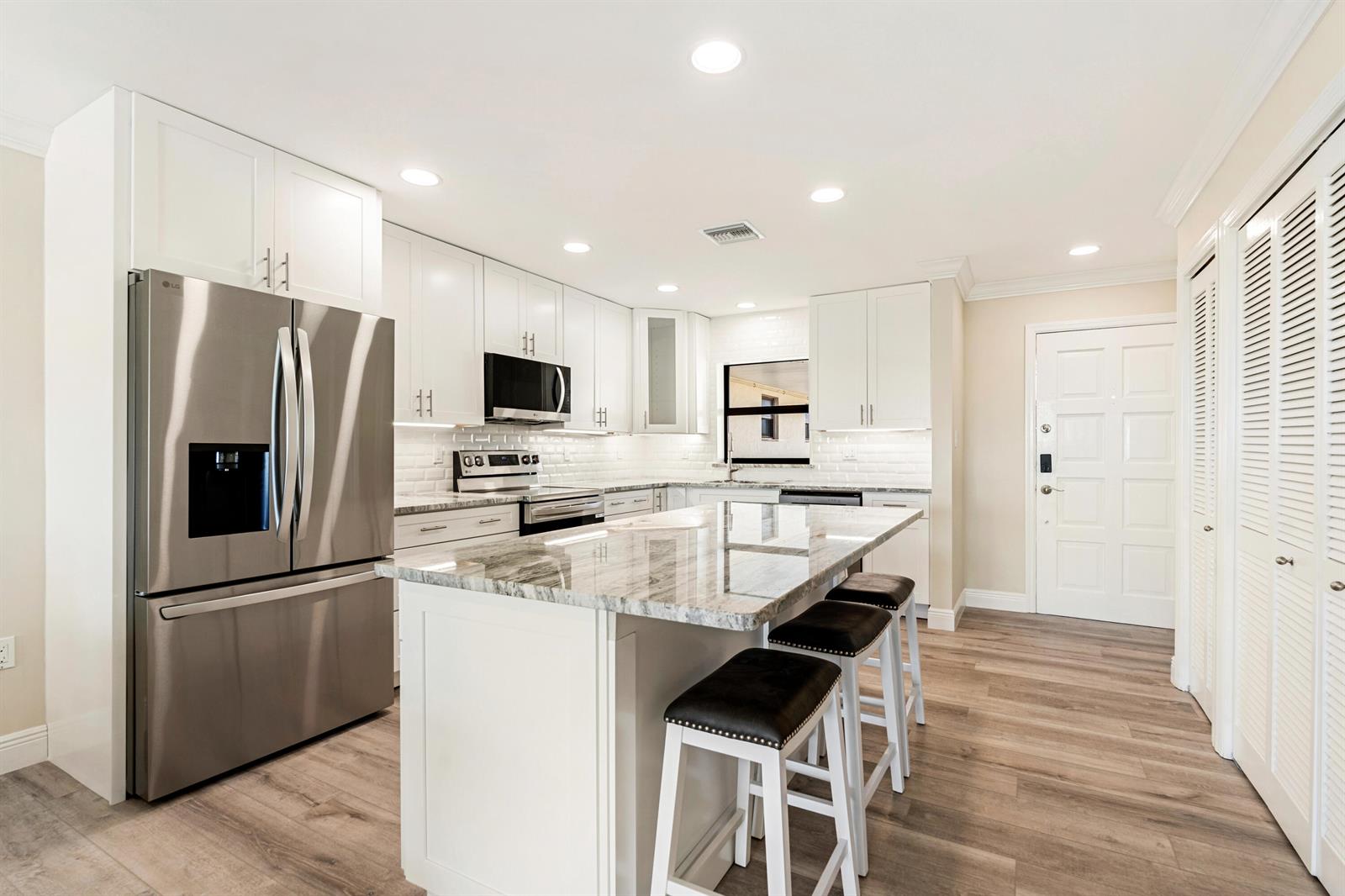 A modern kitchen features white cabinetry, stainless steel appliances, a granite-topped island, and wood flooring — 5300 Highway A1a # 408, Vero Beach FL 32963, VERO BEACH, FL