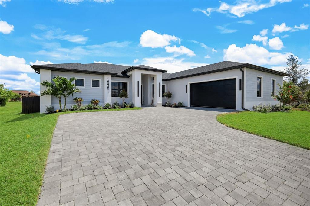 A modern single-story house with a paved driveway, gray siding, and a black garage door — 15301 ACORN CIRCLE, PORT CHARLOTTE, FL