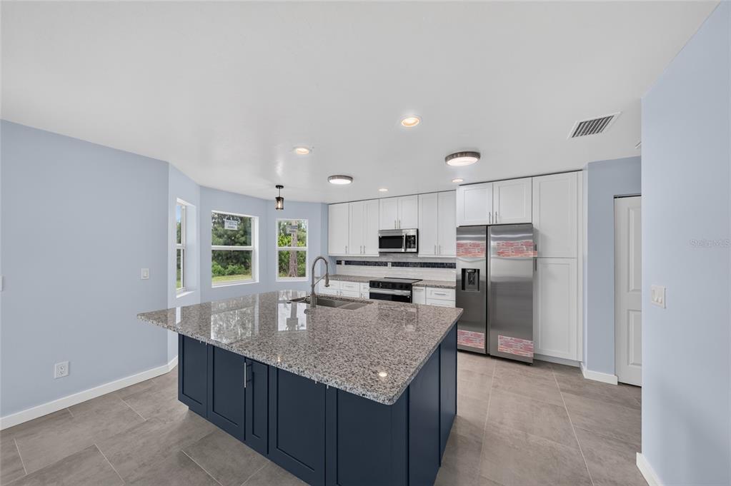 A kitchen with a dark blue island, granite countertops, white cabinets, and stainless steel appliances — 428 SW 19TH AVENUE, CAPE CORAL, FL
