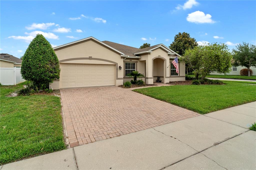 A single-story suburban house with a tan stucco exterior, a two-car garage, and a lawn — 729 MEADOW GLADE DRIVE, WINTER GARDEN, FL
