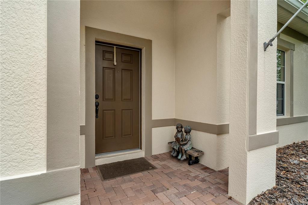 A brown front door with a potted plant and a doormat on a paved porch — 729 MEADOW GLADE DRIVE, WINTER GARDEN, FL