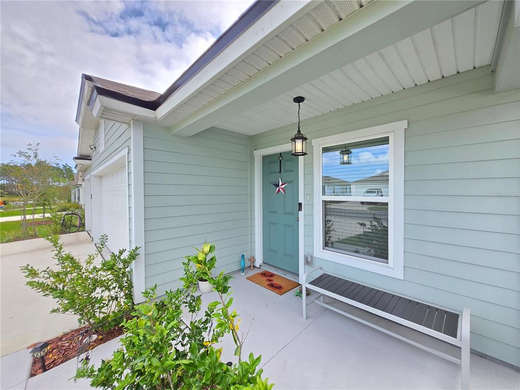 A light green house exterior features a teal front door, a bench, and a small garden — 32 HULETT WOODS ROAD, PALM COAST, FL