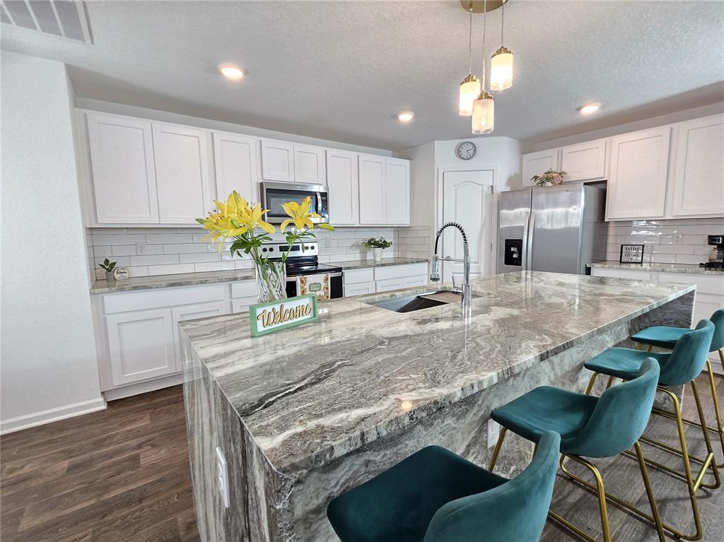 A kitchen features white cabinets, a large stone island with teal stools, and stainless appliances — 32 HULETT WOODS ROAD, PALM COAST, FL