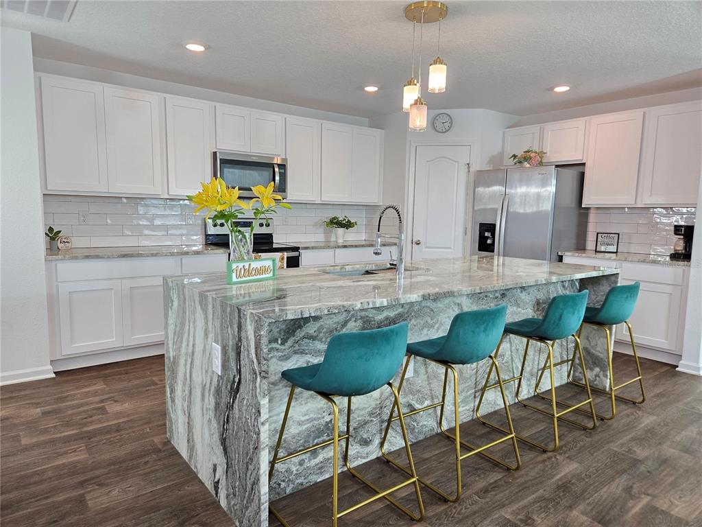 A modern kitchen features white cabinets, a large marble-topped island, and four teal barstools — 32 HULETT WOODS ROAD, PALM COAST, FL