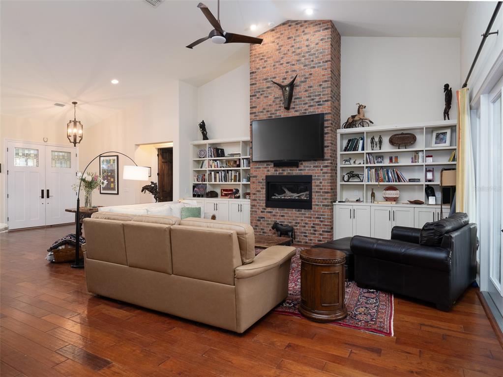 A living room features a brick fireplace, built-in bookshelves, hardwood floors, and a vaulted ceiling — 11130/11122 W HIGHWAY 326, OCALA, FL