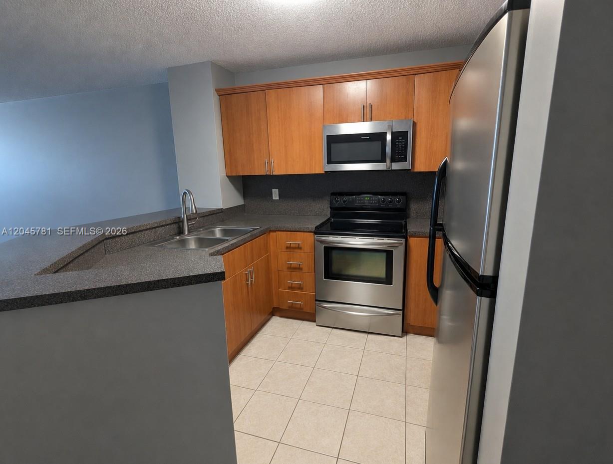 A kitchen with a breakfast bar overlooks an open living area with tile flooring — 8750 N Sherman Cir # 403, Miramar FL 33025, MIRAMAR, FL