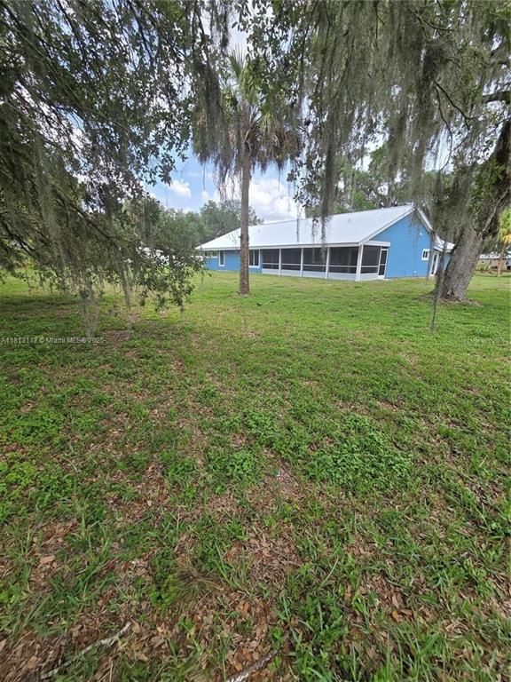 A blue house with a white roof and a screened-in porch sits on a grassy lot — 4508 FIRE COURT, LABELLE, FL