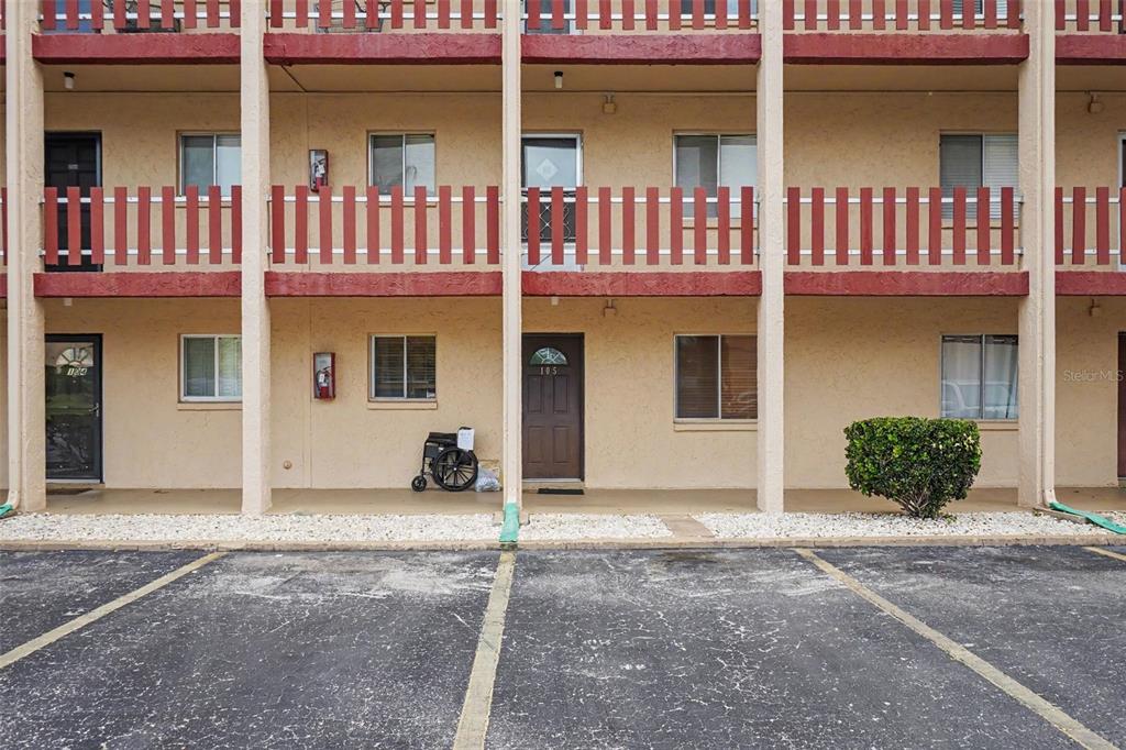 The exterior view shows a two-story apartment building with a ground-level walkway and parking spaces — 4009 LAKE BAYSHORE DRIVE UNIT 105, BRADENTON, FL