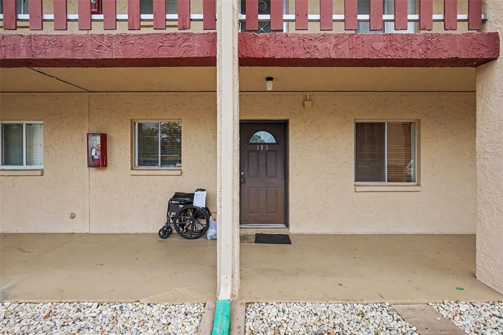 The exterior of a ground-level apartment unit features a brown door numbered 105 — 4009 LAKE BAYSHORE DRIVE UNIT 105, BRADENTON, FL