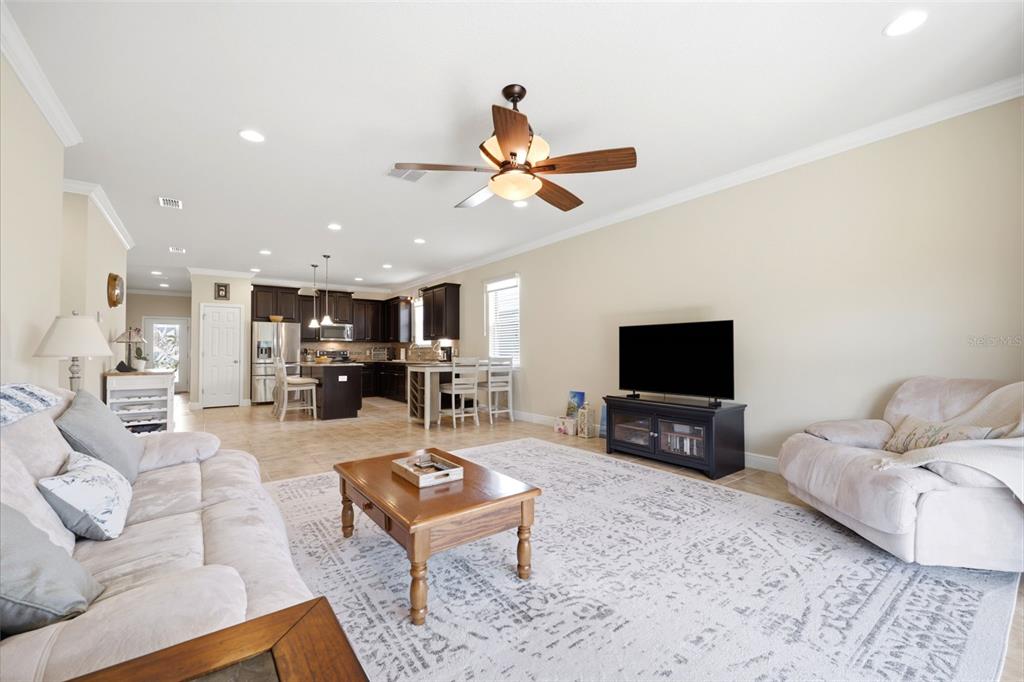 A living room with a ceiling fan, area rug, and television opens to a kitchen — 1707 TRILLIUM BOULEVARD, BROOKSVILLE, FL