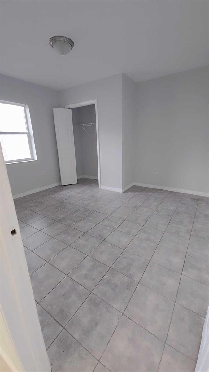 An empty bedroom with gray walls, light tile flooring, and an open closet door — 621 NW 5th Avenue Unit 4, Pompano Beach FL 33060, POMPANO BEACH, FL