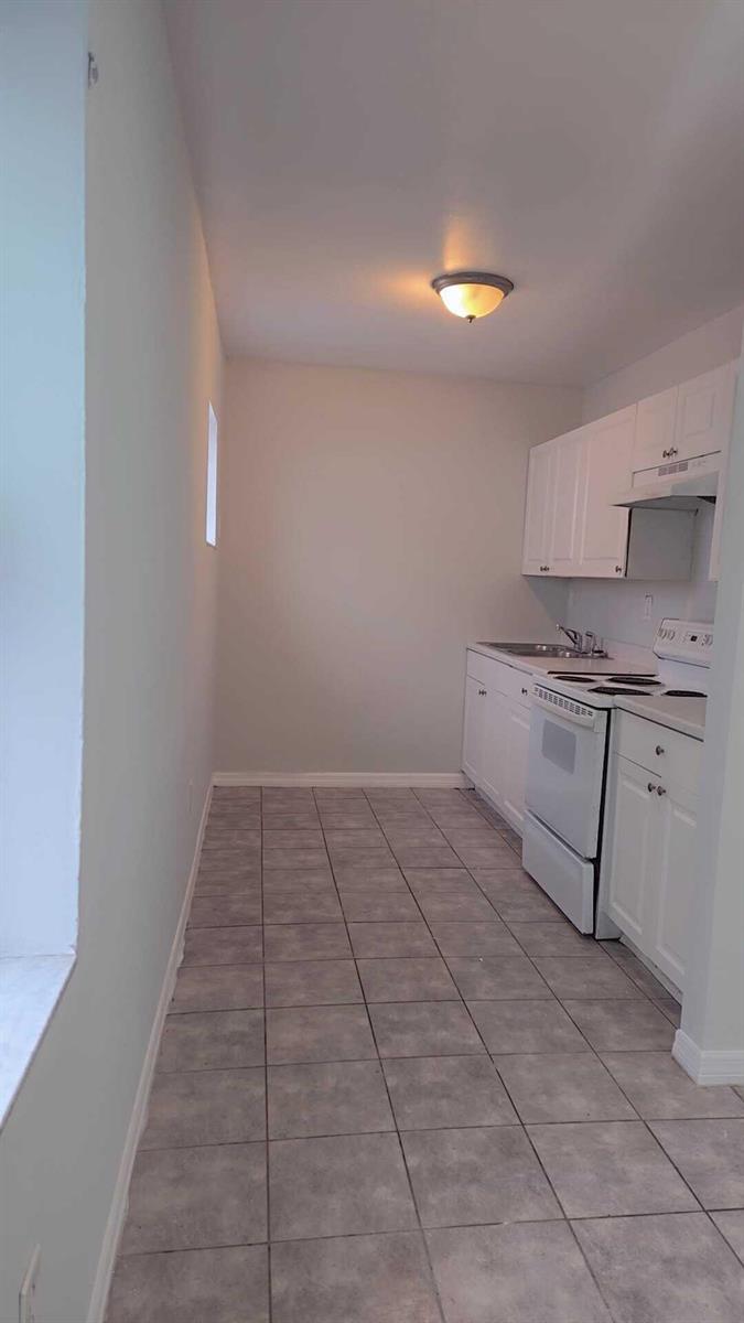 A galley-style kitchen features white cabinets, white appliances, and light-colored tile flooring — 621 NW 5th Avenue Unit 4, Pompano Beach FL 33060, POMPANO BEACH, FL