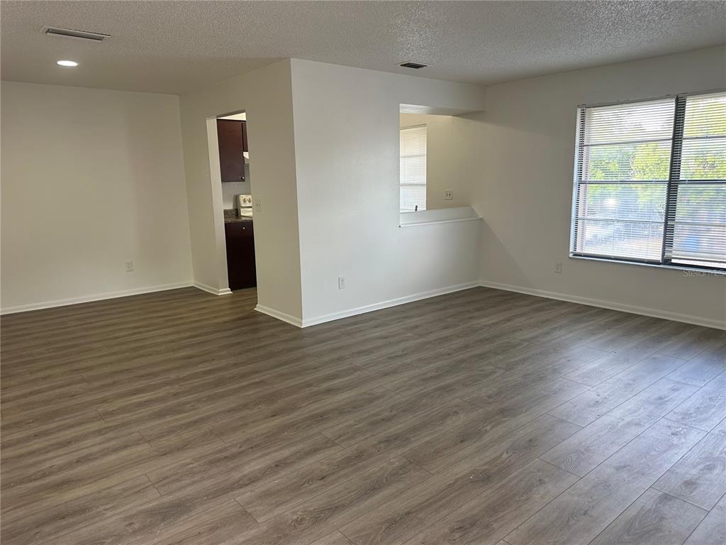 An empty living room features wood-look flooring, white walls, and a pass-through to the kitchen — 8428 CAMDEN STREET UNIT C, TAMPA, FL