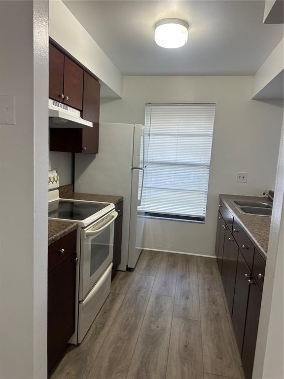 A galley kitchen features dark wood cabinets, laminate countertops, white appliances, and wood-look flooring — 8428 CAMDEN STREET UNIT C, TAMPA, FL